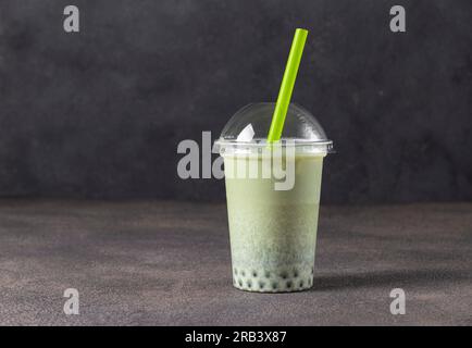 Ein Glas Eistee-Latte mit grünem Matcha zum Mitnehmen, mit Blase auf grauem Hintergrund, Kopierbereich Stockfoto