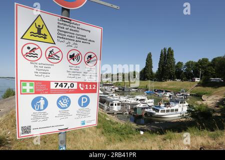 Düsseldorf, Deutschland. 07. Juli 2023. Am Rhein hängt ein Warnschild. Mit neuen Schildern warnt die Stadt Düsseldorf vor dem Schwimmen im Rhein. In den letzten Tagen hat die Feuerwehr im Namen der Stadt neue Warnschilder an den Ufern des Flusses angebracht, die unter anderem auf die gefährliche Strömung in mehreren Sprachen hinweisen. Kredit: David Young/dpa/Alamy Live News Stockfoto