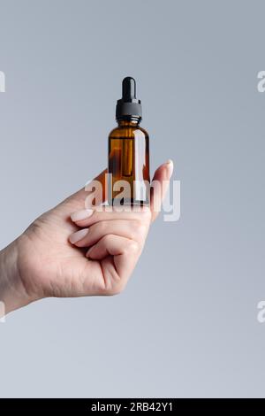 Schöne gepflegte Frauenhand mit brauner Serumflasche auf grauem Hintergrund. Stockfoto