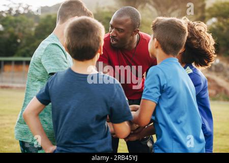 Männlicher Trainer mit seinem Rugby-Team. Sportlehrer, der seinen Schülern einen Motivationsvortrag auf einem Feld hält. Ein Mann, der eine Gruppe betreut Stockfoto