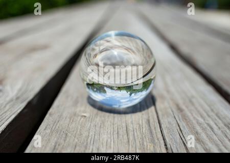 Glaskugel auf verwitterten Holzbrettern reflektiert Bäume und blauen Himmel, weicher Fokus Nahaufnahme Stockfoto