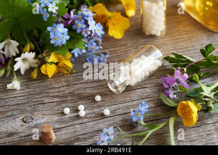 Homöopathische Pillen aus einer Glasflasche, mit frischen bunten Blumen Stockfoto