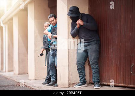 Polizei, Kriminelle und Waffen, die außerhalb des Hauses Schutz, Verstärkung oder Strafverfolgung suchen. Mann, Polizistin und gefährlicher Räuber mit Waffe im Verbrechen Stockfoto