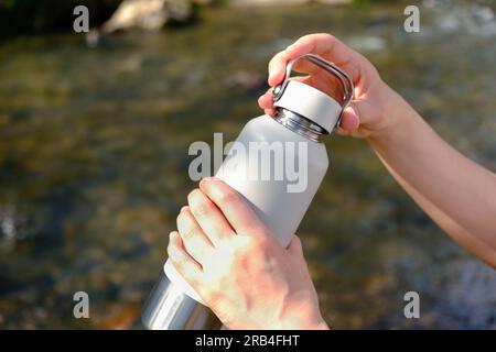 Nahaufnahme, die Hände der Frau halten eine isolierte wiederverwendbare Wasserflasche statt eines einmal-Plastikbechers, öffnen Sie den Deckel, um ihr Wasser zu trinken. Umweltfreundlich, kein Abfall Stockfoto