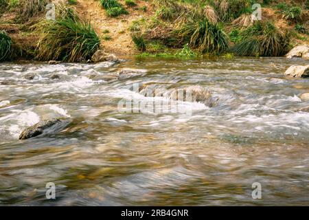 Schneller und kraftvoller Wasserfluss zwischen großen Felsen, Nahaufnahme. Felsbrocken im kalten Bergfluss. Natürlicher Hintergrund Stockfoto