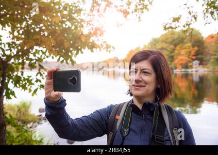 Brünette Touristen machen im Herbst ein Selfie am Ufer eines Sees Stockfoto
