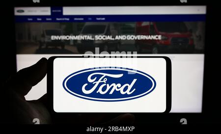 Person, die ein Mobiltelefon mit dem Logo des amerikanischen Automobilherstellers Ford Motor Company auf dem Bildschirm vor der Webseite hält. Konzentrieren Sie sich auf das Display des Telefons. Stockfoto