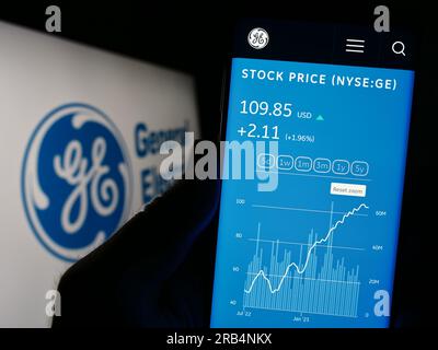 Person, die ein Mobiltelefon mit einer Website des US-Konglomerats General Electric Company (GE) auf dem Bildschirm mit Logo hält. Konzentrieren Sie sich auf die Mitte des Telefondisplays. Stockfoto