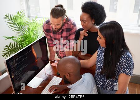Overhead-Foto von vier Entwicklern, die zusammen den Code auf einem großen Bildschirm überprüfen Stockfoto