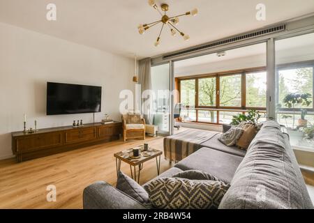 Ein Wohnzimmer mit Holzfußboden und Glasschiebetüren, die auf den Balkon mit Blick auf den Garten gehen Stockfoto