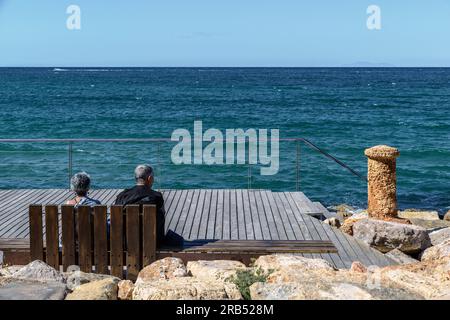 Ein Paar sitzt auf einer Bank am Aussichtspunkt des Küstenpfads (Cami de Ronda), einer Route von Salou nach Llosa in der Provinz Tarragona, Katalonien, Sp Stockfoto