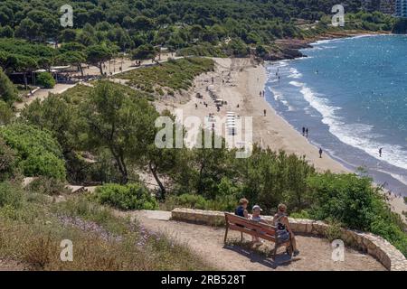 Drei Personen sitzen auf einer Bank mit Blick auf den Küstenweg Platja Llarga (langer Strand) (Cami de Ronda) Salou, Tarragona, goldene Küste, Spanien, Europa. Stockfoto