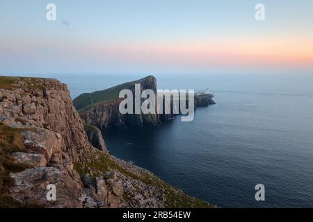 Eine Landschaft eines feinen Leuchtturms, der auf einer atemberaubenden Klippe vor dem Hintergrund des Meeres steht und von der untergehenden Sonne beleuchtet wird. Neist Point, Isle of Skye, Schottland Stockfoto