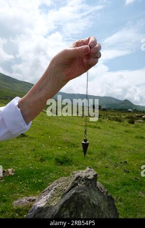 Weibliche Wanderer, die ein Pendel über einem stehenden Stein am Steinkreis von Ardgroom, County Cork, Irland, hält - John Gollop Stockfoto