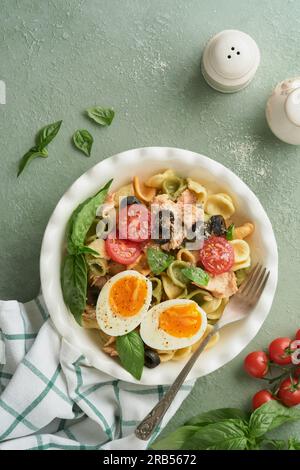 Italienischer Nudelsalat. Orekchiette-Pasta mit Thunfisch, Tomatenkirsche, Oliven, Basilikum und Parmesan auf grünem Stein- oder Betonboden. Trad Stockfoto