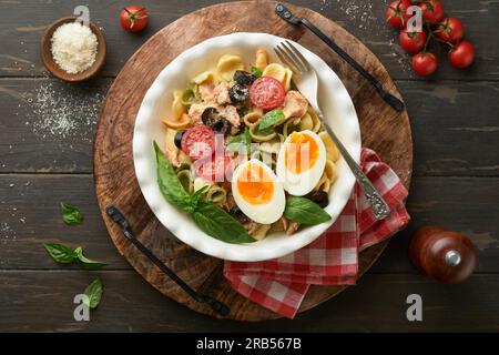 Italienischer Nudelsalat. Orekchiette Pasta mit Thunfisch, Tomatenkirsche, Oliven, Basilikum und Parmesan auf einem dunklen Holztisch mit altem rustikalem Hintergrund. Stockfoto