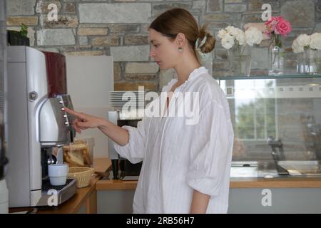 Frau, die Kaffee mit der Kaffeemaschine in der Selbstbedienungs-Cafeteria macht Stockfoto