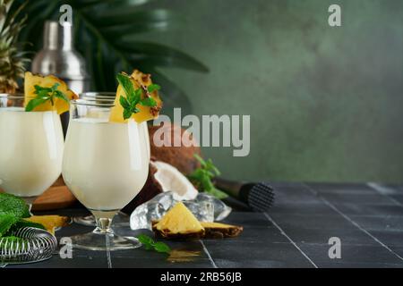 Pina Colada. Traditioneller karibischer Cocktail aus Rum, Ananassaft und Kokosnusscreme mit tropischen Früchten und Barutensilien auf frischem grünen Hintergrund. Stockfoto