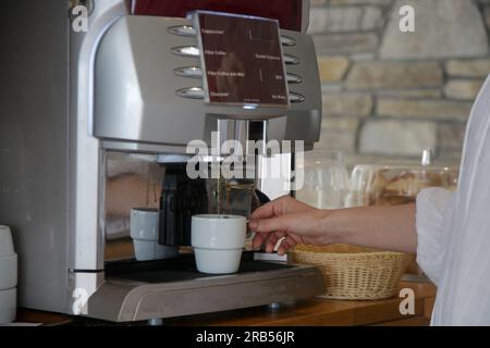 Frau, die Kaffee mit der Kaffeemaschine in der Selbstbedienungs-Cafeteria macht Stockfoto