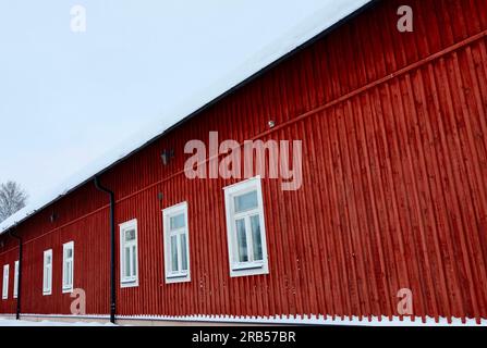 Seitenperspektive Sicht auf die alte rot lackierte Holzbauwand mit den Fenstern mit dem weißen Rollladenrahmen Stockfoto