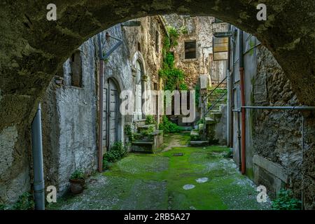 Innenhof mit Bogeneingang mit Moos auf dem Boden und Steinhäusern im mittelalterlichen Dorf Tocco da Casauria. Tocco da Casauria, Abruzzen Stockfoto