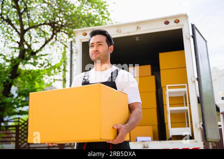 Ein glücklicher Zusteller hält die Kiste vor dem Lieferwagen, der Zusteller überprüft den Umzugsservice und den Umzugsservice Stockfoto