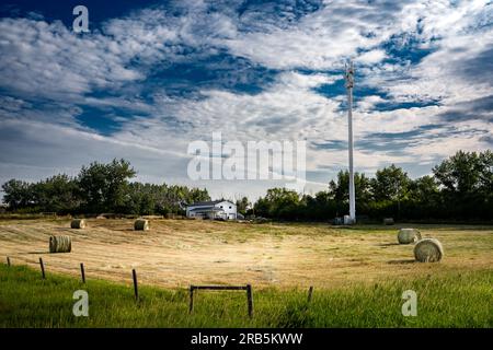 Handyturm mit Blick auf runde Strohballen auf einem kleinen Hof mit Stacheldrahtzaun im Rocky View County Alberta, Kanada. Stockfoto