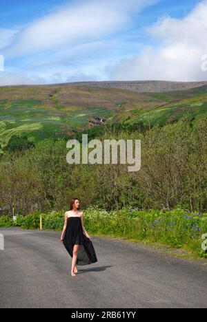 Eine Frau in fließendem, schwarzem Kleid geht den Weg entlang am Mt. Esja, Island. Stockfoto