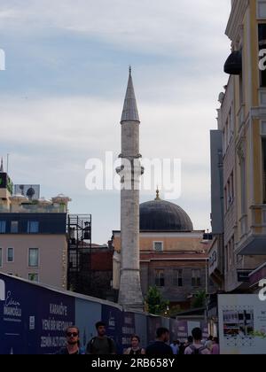 Kleine und einfache Moschee im Karakoy-Viertel von Istanbul neben einem Gebäude mit Dachterrasse, während die Leute auf der Straße laufen. Istanbul Stockfoto