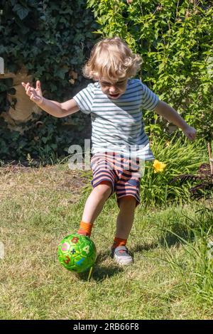 Ein kleiner Junge tritt einen Ball im Sommergarten Stockfoto