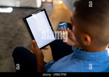 Birassischer Mann, der Medikamente in der Hand hält und zu Hause Videoanrufe mit einem Tablet mit Kopierbereich auf dem Bildschirm tätigt. Medizinische Dienste, Kommunikation, Telemedizin und er Stockfoto