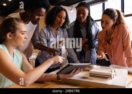 Diverse Architekteninnen in der Diskussion mit Modell und Tablet in zwangloser Bürobesprechung. Gelegenheitsbüro, Teamwork, Business, Lifestyle, kreative Arbeit, Stockfoto