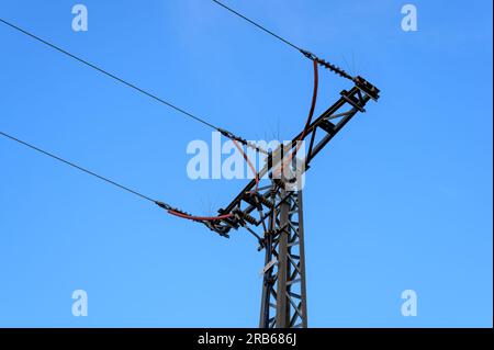 Ein dreiphasiger Netzleitungspylon wird zu einem Massekabel mit Anti-Vogel-Spikes oben und rot isolierten Kabeln, die nach unten übertragen werden, abgeschlossen. Stellen Sie einen ein Stockfoto