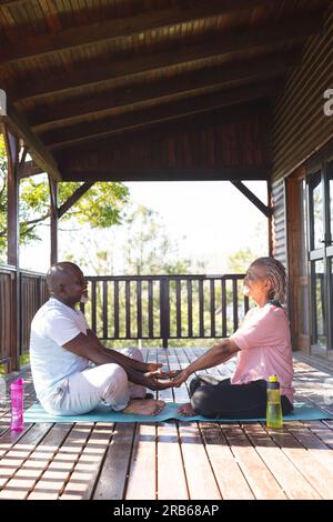 Glückliches Senior-afroamerikanisches Paar, das Yoga auf der Matte auf der Terrasse praktiziert. Seniorenleben, Entspannung, Ruhestand, gesundes Leben, Fitness, Bewegung und wir Stockfoto