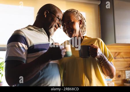Glückliches Senior-afroamerikanisches Paar, das zu Hause Kaffee trinkt und umarmt. Seniorenleben, Entspannung und Ruhestand, unverändert. Stockfoto