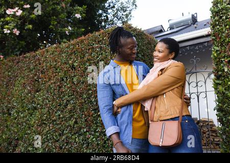Glückliches afroamerikanisches Paar, das vor dem Haus Efeu umarmt und steht. Unverfälscht, Liebe, Zusammensein, glücklich, Jacke, Romantisches und Lifestyle-Konzert Stockfoto
