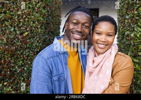 Portrait eines glücklichen jungen afroamerikanischen Paares, das vor dem Haus über Efeu steht. Unverändertes, Liebe, Zusammensein, Glück, Jacke und Lifestyle-Konzept. Stockfoto