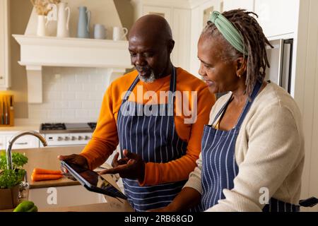 Glückliches afroamerikanisches Seniorenpaar, das Gemüse zubereitet und ein Tablet in der Küche benutzt. Seniorenleben, Essen, Kochen, Kommunikation, Ruhestand, Tog Stockfoto