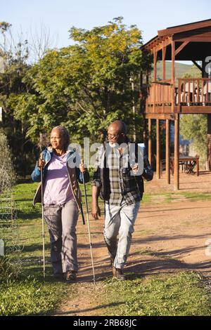 Ältere afroamerikanische Paare mit Rucksäcken, die in sonniger Natur spazieren gehen. Seniorenleben, Entspannung, Wohlbefinden in der Natur und Ruhestand, unverändert. Stockfoto