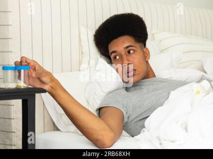 Ein birassischer Mann, der im Bett liegt und nach Medikamenten greift. Medizin, Gesundheitswesen, Wohlbefinden, Lebensstil und häusliches Leben, unverändert. Stockfoto