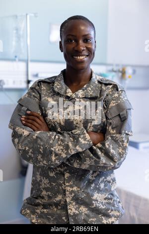Porträt einer glücklichen afroamerikanischen Soldatin, die Militäruniform trägt und im Krankenhaus Waffen kreuzt. Krankenhaus, Medizin, Gesundheitswesen, Gesundheitswesen Servi Stockfoto