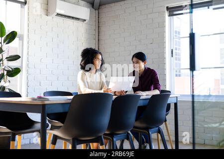 Zwei verschiedene weibliche Geschäftskollegen erörtern Dokumente im Besprechungsraum des Büros. Teamarbeit, Arbeit, Arbeit, Meeting und zwangloses Büro, unveränderlich Stockfoto