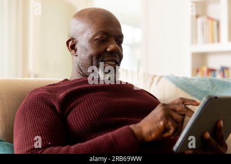 Glücklicher afroamerikanischer Seniorist, der ein Tablet im sonnigen Wohnzimmer benutzt. Seniorenleben, Ruhestand, Kommunikation und häusliches Leben, unverändert. Stockfoto
