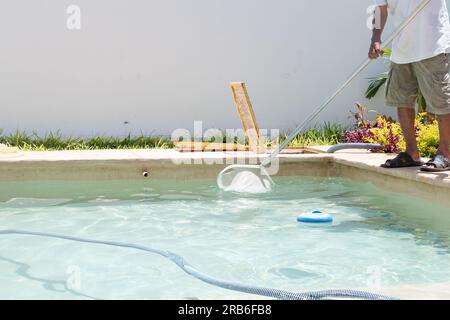 Ein Lateiner putzt an einem sonnigen Tag einen Gartenpool mit Netz und Staubsauger. Stockfoto