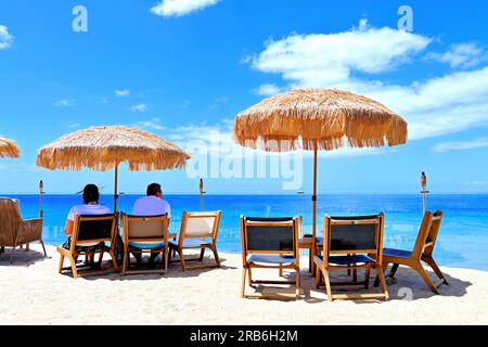 Lanzarote Kanarische Inseln Puerta del Carmen Hauptstrand und Palmen und Strohschirme sitzen und genießen die Aussicht mit blauem Himmel und Meer Stockfoto