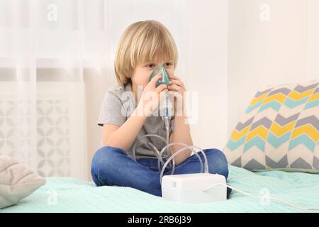 Kranker kleiner Junge mit Vernebler zur Inhalation am Bett zu Hause Stockfoto