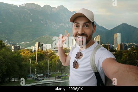 Ein lächelnder Mann, der Selfie macht und ein Friedenszeichen gegen das Stadtbild zeigt Stockfoto