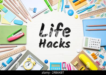 Words Life Hacks, umgeben von Schreibwaren auf weißem Holztisch, flach liegend Stockfoto