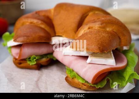 Leckere Sichelrolle mit Brie, Schinken und Salat auf Pergamentpapier, Nahaufnahme Stockfoto