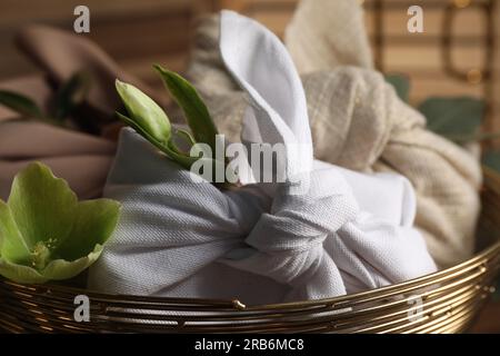 Furoshiki-Technik. Geschenke verpackt in verschiedenen Stoffen und Blumen in Schüssel, Nahaufnahme. Stockfoto